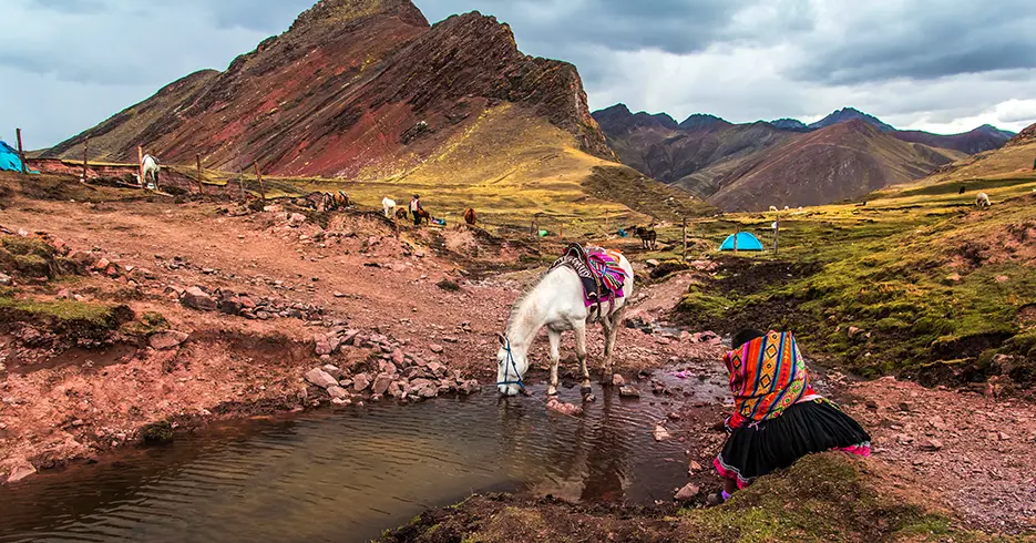 Cavalos descansando na rota da montanha das 7 cores, um bebendo água com seu dono sentado descansando, vista das montanhas.