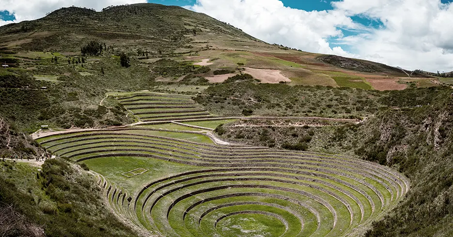 cusco o que fazer Vista dos terraços circulares de Moray, antigo sítio inca, rodeado de montanhas e vegetação, com céu claro.