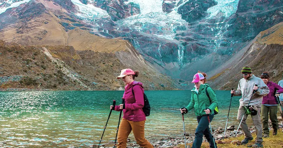 o que fazer em cusco peru: Turistas em uma caminhada com seus bastões de caminhada na lagoa Humantay, águas cristalinas azul-turquesa e a montanha coberta de neve de Humantay no topo
