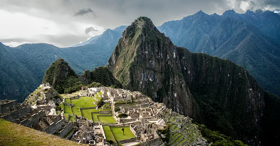 Vista de Machu Picchu, com suas estruturas de pedra cercadas por montanhas verdes e um céu parcialmente nublado