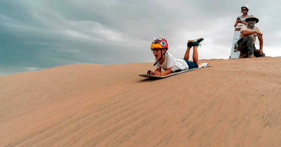 Menino praticando sandboard nas dunas de Huacachina em Ica