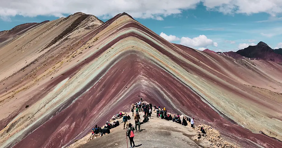O que fazer em Cusco Peru A montanha das 7 cores nos pontos turísticos para visitar em Cusco Peru, com cores como vermelho, amarelo, verde e um céu azul claro com vários turistas ao fundo