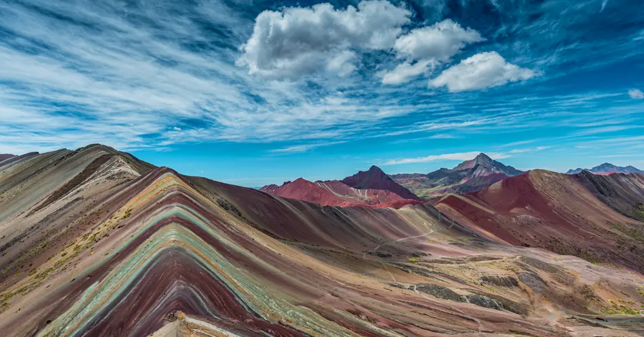 Paisagem da montanha de 7 cores, um caminho com pedras e terra e muitas montanhas de cores diferentes, como vermelho, verde e amarelo com um céu azul e nuvens brancas