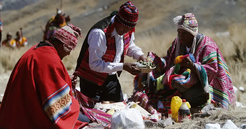 Três homens realizando cerimônia em homenagem à Pachamama, rodeados de paisagens e vestidos com roupas típicas peruanas