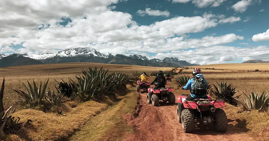 Rota para as minas de sal de Maras em quadriciclos com vista para uma montanha nevada ao fundo e plantas na área e um céu azul claro