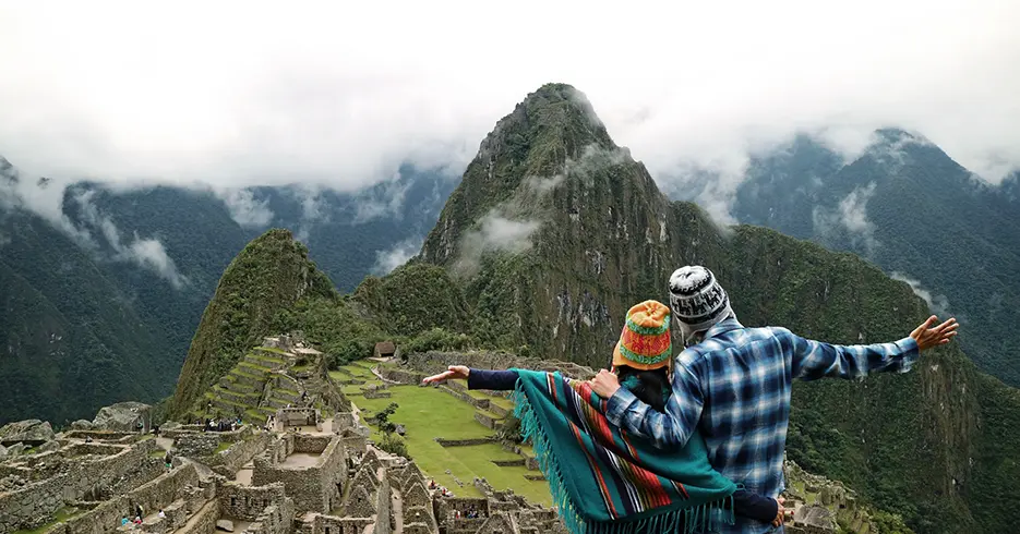Turistas posando com Machu Picchu ao fundo e um céu nublado e as estruturas Incas na parte inferior