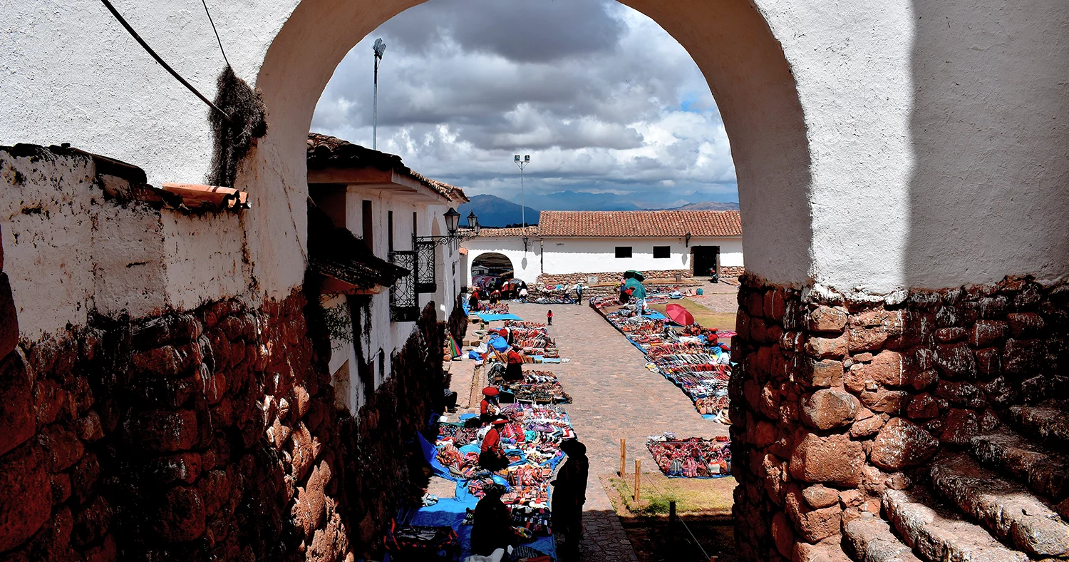 Traditional handicraft market in Chinchero, Cusco, with colorful Andean textiles displayed beneath a colonial arch