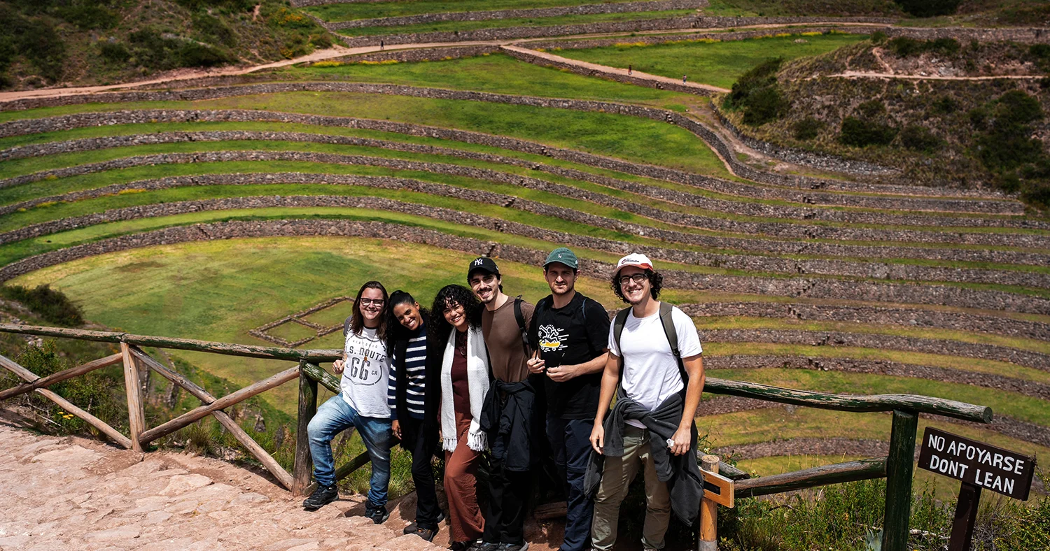 Five travelers posing at the Moray archaeological site with circular Inca terraces in the background
