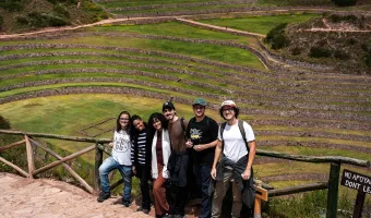 Five travelers posing at the Moray archaeological site with circular Inca terraces in the background
