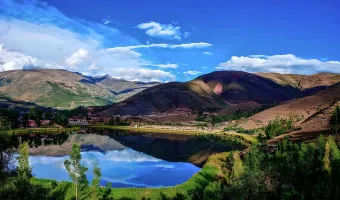 Panoramic view of Urcos Lake reflecting the surrounding Andean hills and blue sky near Cusco, Peru